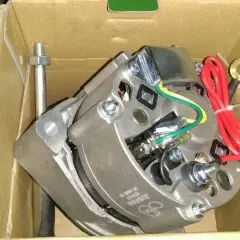 Nowy alternator C-330 w pudełku, gotowy do podłączenia. Widać przewody i mocowania.