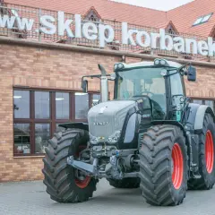 Potężny traktor Fendt 936 z czerwonymi felgami stoi przed budynkiem z napisem "www.sklepkorbanek.pl".